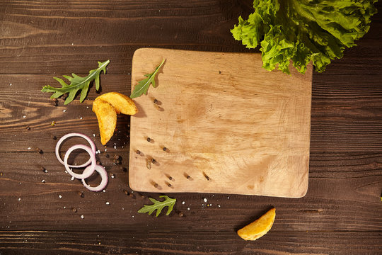 around wooden board scattered potatoes, onions, lettuce, arugula, pepper. Free space for text. Wooden background for food design or restaurant menu. Flatlay.