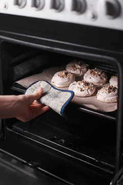 woman's hand pulls out meringue with walnuts  on baker paper from oven. close-up