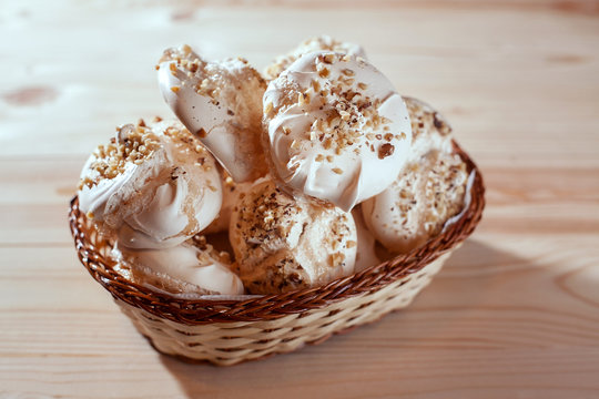 meringue with nuts in basket on wooden background on bright morning