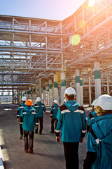 Workers of chemical factory in working clothes walks near large pipeline construction to their...