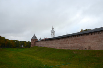 Red wall of the Kremlin with a corner tower next to a moat covered with grass. Veliky Novgorod, Russia.