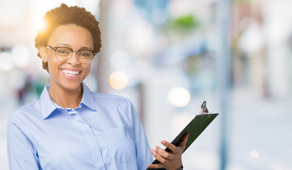 Young african american businesss woman holding clipboard over isolated background with a happy face...