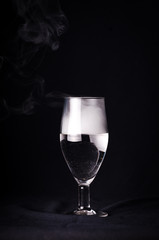  Silhouette wine glasses. A champagne glass filled with champagne on a black background and with beautiful voluminous highlights. A glass filled with smoke that comes out of it on a black background.
