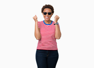 Beautiful young african american woman wearing sunglasses over isolated background celebrating surprised and amazed for success with arms raised and open eyes. Winner concept.