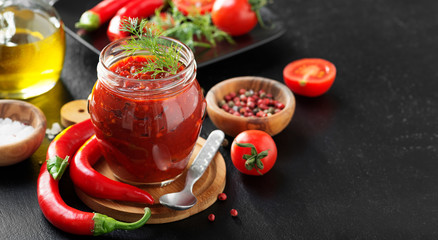 Traditional  chili sauce in a glass jar with fresh herbs, tomatoes and olive oil.