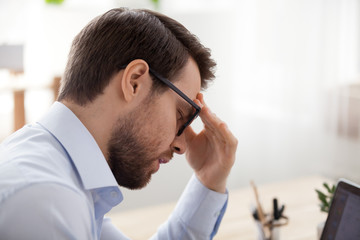 Stressed male employee sit with eyes closed suffering from headache or dizziness, ill man feel...
