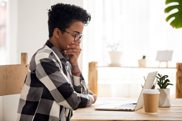 Stressed African American female in glasses look at laptop read bad online news, depressed black girl feel down receive negative response or dismissal email, afro woman upset with message on computer