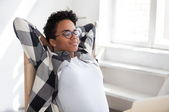 Peaceful African American millennial female in glasses lean back in chair relaxing after working day, calm black woman stretching having break from work at workplace, afro girl rest with eyes closed
