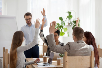 Diverse employees raise hands engaged in teambuilding activity during business mentor or coach...