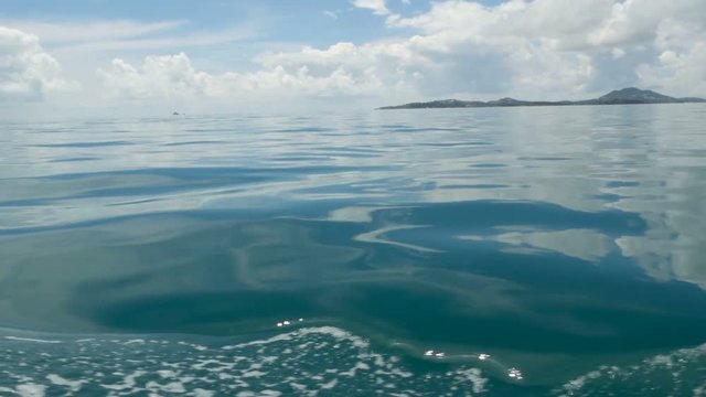 Small foamy blue waves after a boat and calm ocean in cloudy day. Idyllic tropical waterscape. The sky is reflected in the surface of the quite water of the sea. windless weather