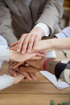 Close up of multiracial workers join hands together in stack show support, reach shared goal, diverse people engaged in teambuilding activity or training at meeting, promise help. Cooperation concept