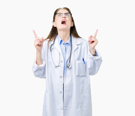 Middle age mature doctor woman wearing medical coat over isolated background amazed and surprised looking up and pointing with fingers and raised arms.