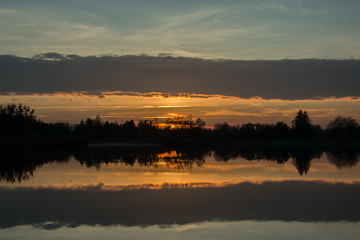 Sunset on the lake, trees on the shore and reflection of cloud in the water