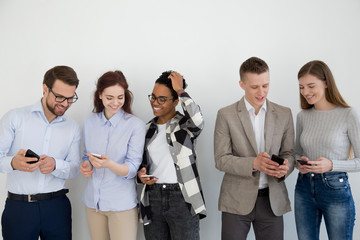 Multiethnic young people stand in row or queue near wall using smartphones, diverse millennial...