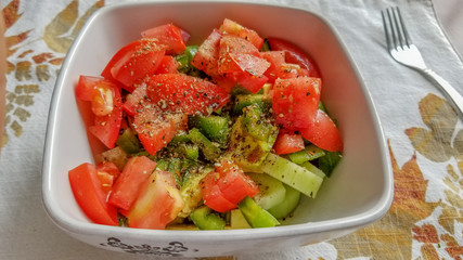 Cucumber and tomato salad with black pepper and herbs, in a white ceramic bowl