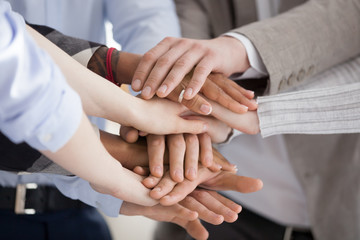 Close up of diverse workers or employees put hands in stack showing support and unity, reach shared goal together, multiracial people engaged in teambuilding activity or training. Teamwork concept