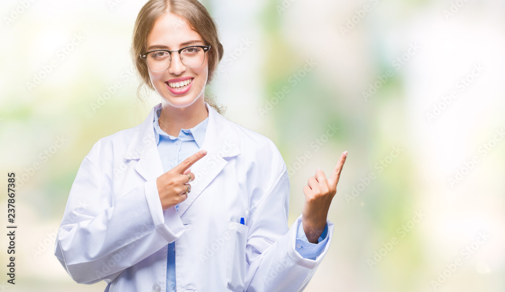 Sticker Beautiful young blonde doctor woman wearing white coat over isolated background smiling and looking at the camera pointing with two hands and fingers to the side.