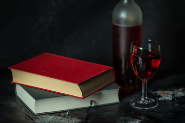 a glass and a bottle of red wine next to books on a black background