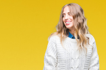 Beautiful young blonde woman wearing winter sweater over isolated background looking away to side with smile on face, natural expression. Laughing confident.