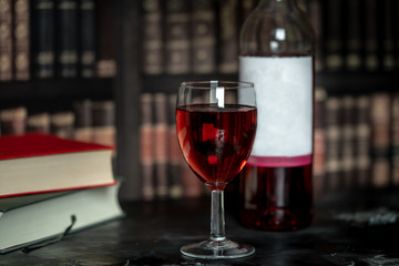 in a room full of books, on the table stands a glass and a bottle of red wine, next to them lies two books