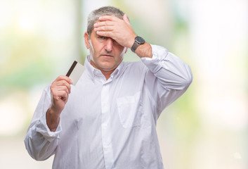 Handsome senior man holding credit card over isolated background stressed with hand on head, shocked with shame and surprise face, angry and frustrated. Fear and upset for mistake.