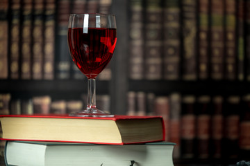 in a room full of books, on the table stands a glass of red wine, next to them lies two books