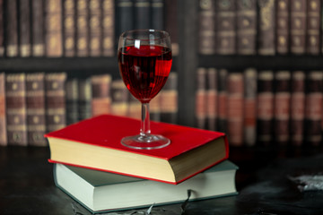 in a room full of books, on the table stands a glass of red wine, next to them lies two books