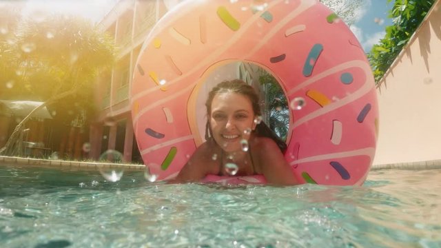Woman with sunglasses in blue bikini lying in inflatable pink donut float in pool on sunny summer day. Look at camera. Woman bikini swimming pool on watermelon rubber ring relaxing vacation