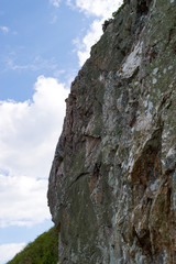 Sheer steep rocky cliff face in Wicklow, Ireland with blue sky and white clouds background