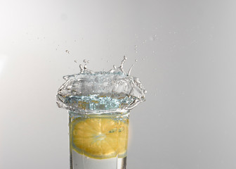 A glass of lemonade on a light background with splashing water