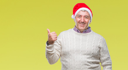 Fototapeta premium Handsome senior man wearing christmas hat over isolated background smiling with happy face looking and pointing to the side with thumb up.