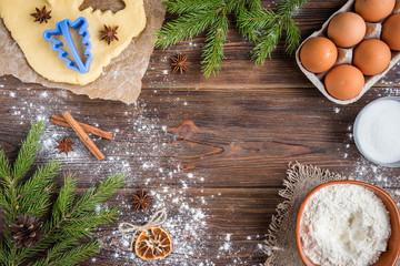 Christmas baking of ginger cookies on dark wooden background with fir branches.