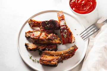 Bbq pork ribs with chili sauce on white plate. Pork ribs on slate background. Copy space.