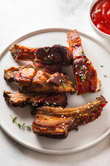 Bbq pork ribs with chili sauce on white plate. Pork ribs on slate background. Copy space.