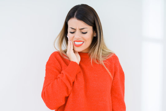Young woman wearing casual red sweater over isolated background touching mouth with hand with painful expression because of toothache or dental illness on teeth. Dentist concept.