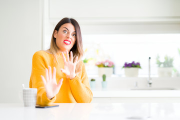 Young beautiful woman drinking a cup of coffee at home disgusted expression, displeased and fearful doing disgust face because aversion reaction. With hands raised. Annoying concept.