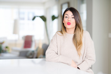 Young beautiful woman wearing winter sweater at home puffing cheeks with funny face. Mouth inflated with air, crazy expression.