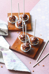 Chocolate Cake Pops sprinkled with nuts, on little wooden plate, on grey brown background.
