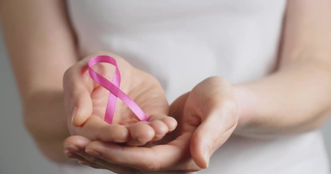 Woman holding a pink ribbon in her hands, symbolizing breast cancer awareness.