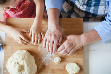 Hands of child and old retired woman. Grandmother and granddaughter are cooking in home kitchen. Family roll out dough for bakering. Senior woman and kid girl are preparing for Thanksgiving Day dinner