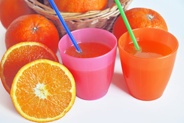 dissetante spremuta di arance dentro due bicchieri colorati, pronta da bere con due cannucce, vicino una arancia tagliata