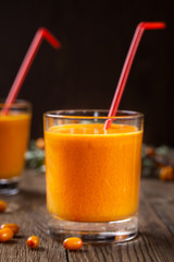 Two glasses of sea buckthorn juice with sea buckthorn berries in the foreground. Dark background