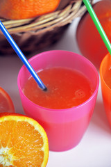dissetante spremuta di arance dentro due bicchieri colorati, pronta da bere con due cannucce, vicino una arancia tagliata