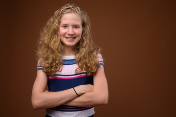 Young beautiful blonde teenage girl smiling against brown background