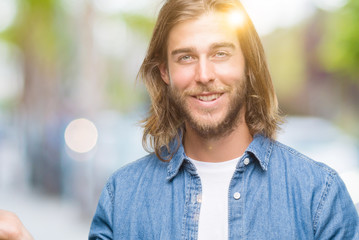 Young handsome man with long hair over isolated background amazed and smiling to the camera while presenting with hand and pointing with finger.