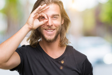 Young handsome man with long hair over isolated background doing ok gesture with hand smiling, eye looking through fingers with happy face.