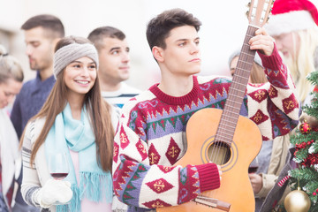 Young man with friends playing guitar on balcony on Christmas