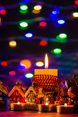 Christmas decorations. Toy house and colored balls with bokeh. Christmas decorations on blurred background. Burning candles and Christmas tree branch. Vintage style