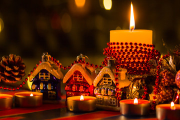 Christmas decorations. Toy house and colored balls with bokeh. Christmas decorations on blurred background. Burning candles and Christmas tree branch. Vintage style
