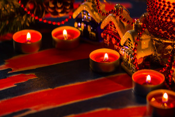 Christmas decorations. Toy house and colored balls with bokeh. Christmas decorations on blurred background. Burning candles and Christmas tree branch. Vintage style